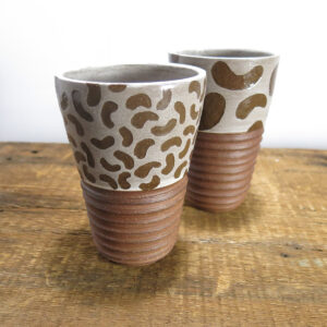 Tumbler made of red clay. Pattern made of bean shapes on the top in white, texture on the bottom part of the cup.