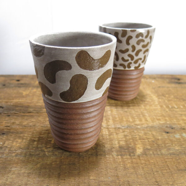 Tumbler made of red clay. Pattern made of large bean shapes on the top in white, texture on the bottom part of the cup.
