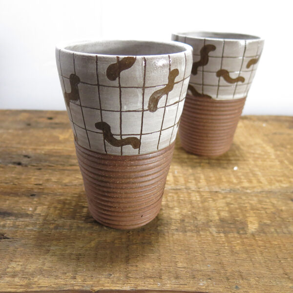 Two red clay ceramic tumblers with a pattern of worms on a grid.