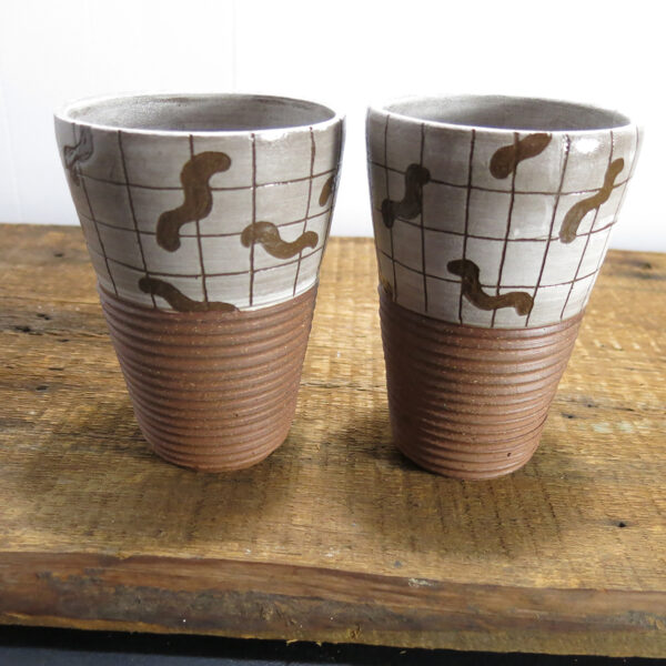Two red clay ceramic tumblers with a pattern of worms on a grid, side by side.