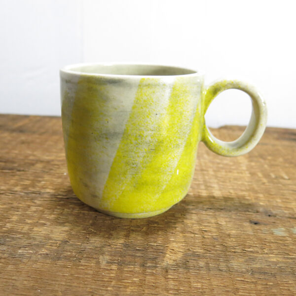 White ceramic mug with round handle, rubbed grey texture and sprayed faint yellow decoration.