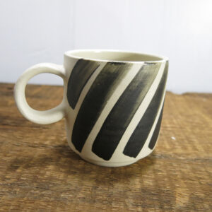 White stoneware cup with round handle, decorated with black painted stripes.
