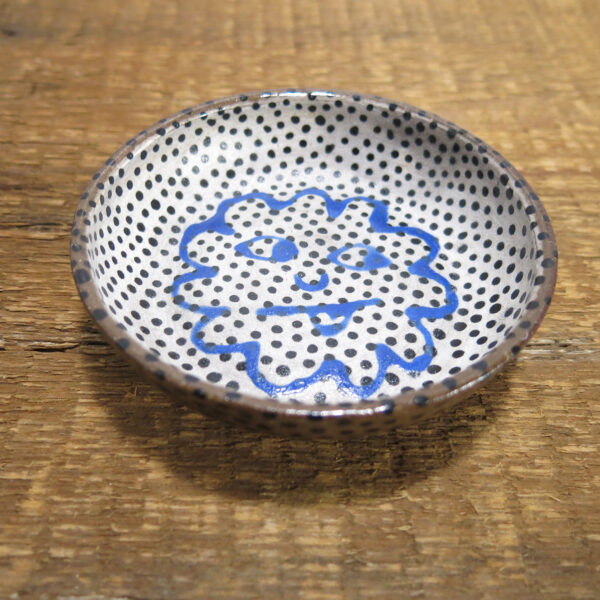 Ceramic sauce bowl with white background, black dots, and a blue cloud face sticking out its tongue.