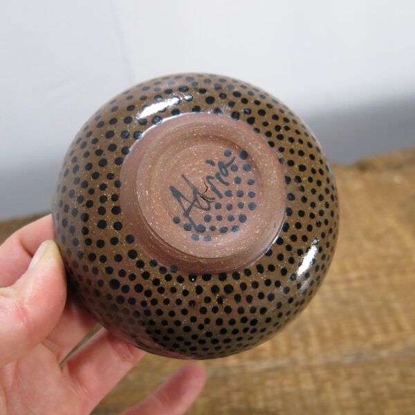 The underside of the cloud face bowl, shows the dark clay and black dots and signature.