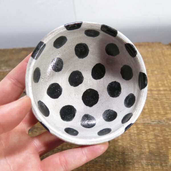 Small ceramic sauce bowl with large black dots on a white background held in a hand.