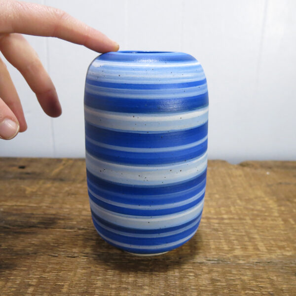 A hand touching a Ceramic vase with blue stripes.