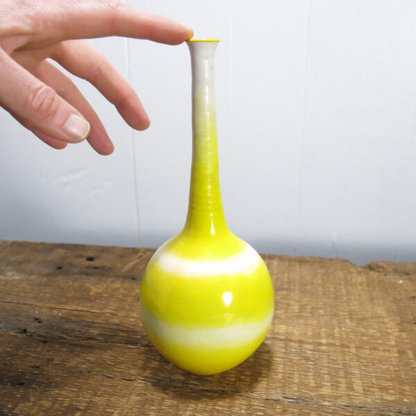 A hand touching a Porcelain vase with a very long, thin neck.