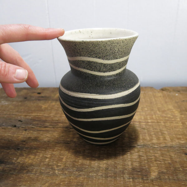 Hand touching a Black and white vase made of speckled clay.
