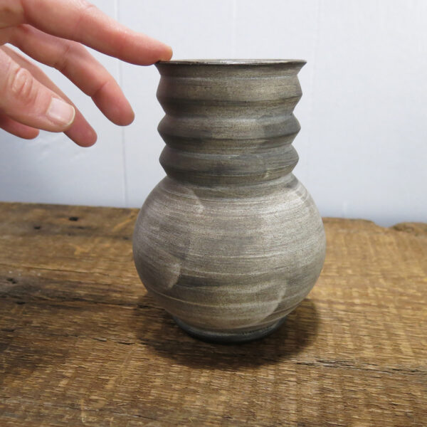 A hand touching a Ceramic vase with a brushed texture.