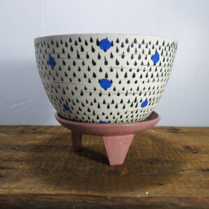 Large ceramic planter with black and blue decoration, sitting on a pink, three-legged ceramic stand.