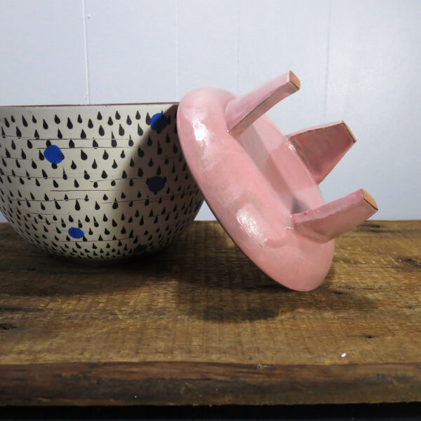 a pink, three-legged ceramic stand upside-down, next to a planter.