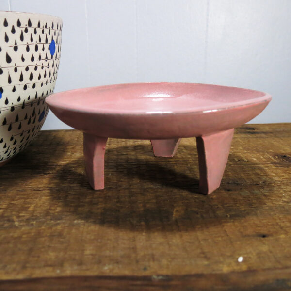 a pink, three-legged ceramic stand next to a planter that is mostly out of the frame.