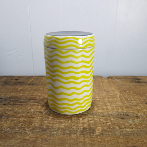Porcelain jar with yellow stripes and a black dot on top of the lid.