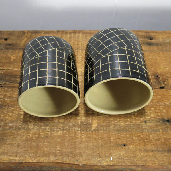Two ceramic cylinder pots with a black and white grid pattern, made of cream-colored clay. They are on their side to show differences in width.
