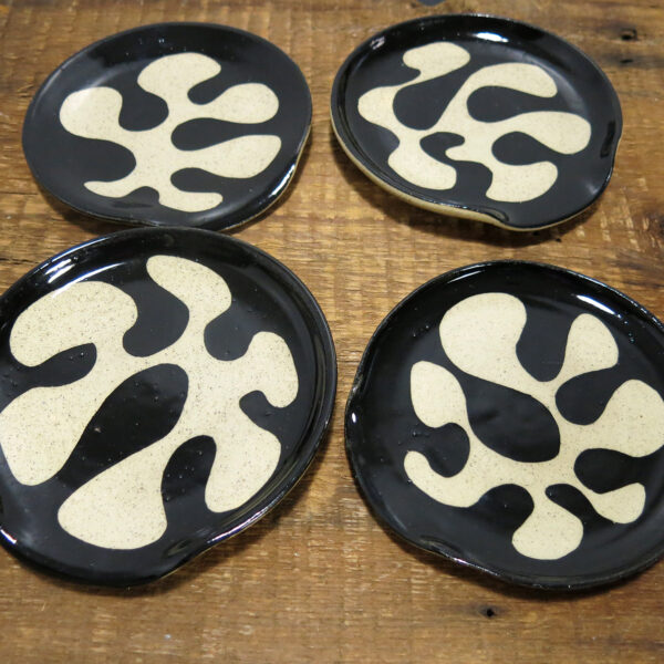 Four buff ceramic spoon rests with an organic black decoration.